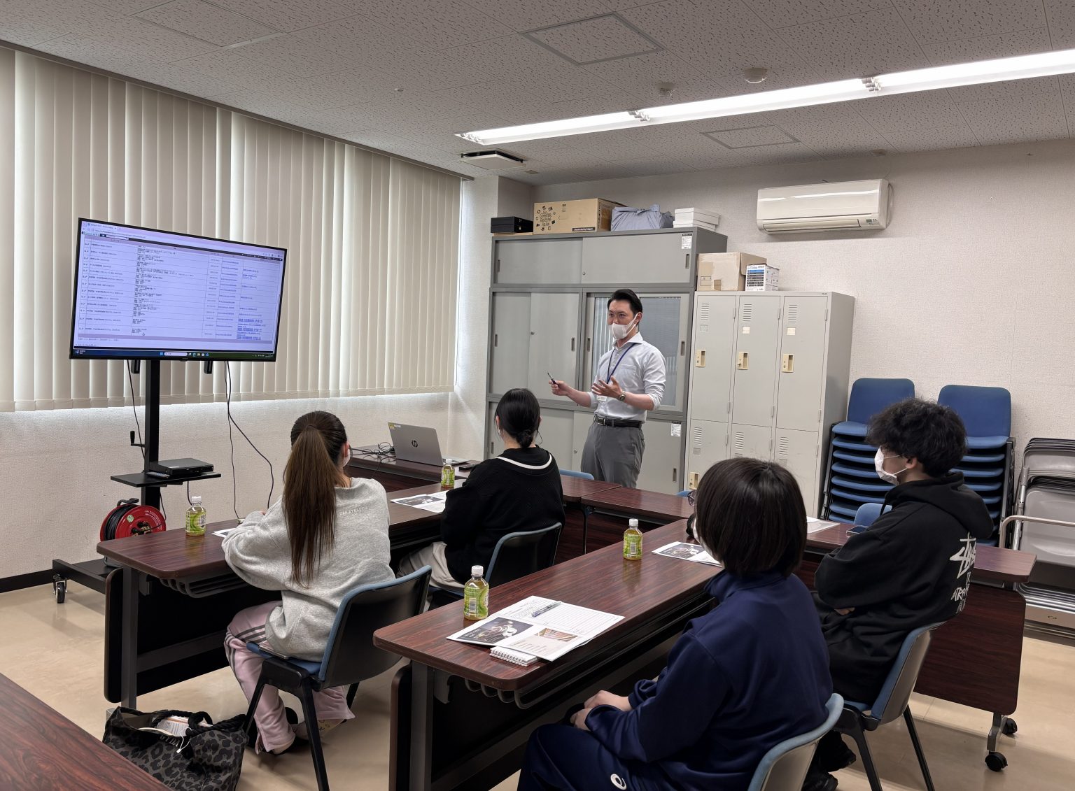 スタッフによる研修・講習会の様子。複数の参加者がテーブルに着席し、講師がプレゼンテーション。